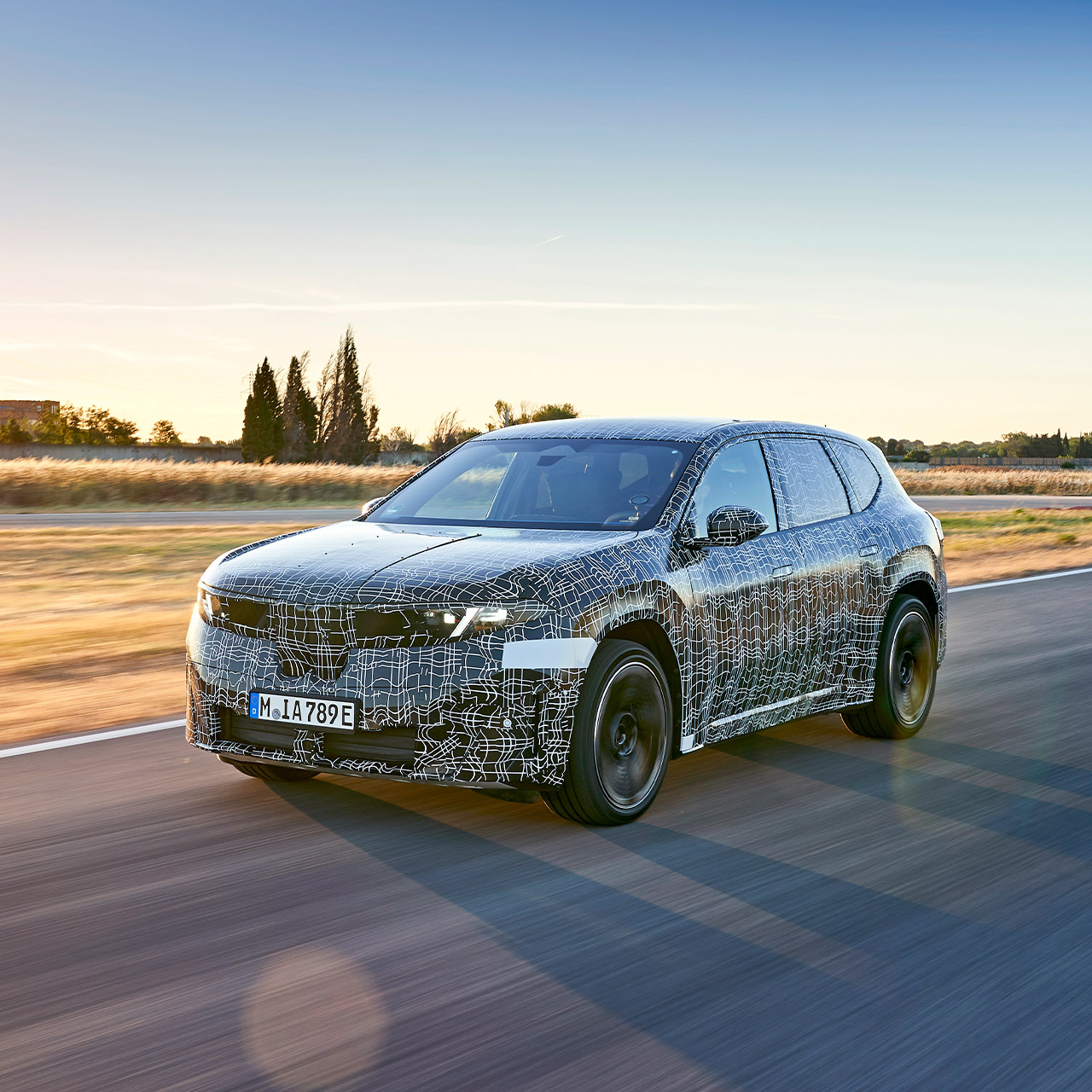 The prototype of the BMW iX3 50 xDrive drives on a country road.