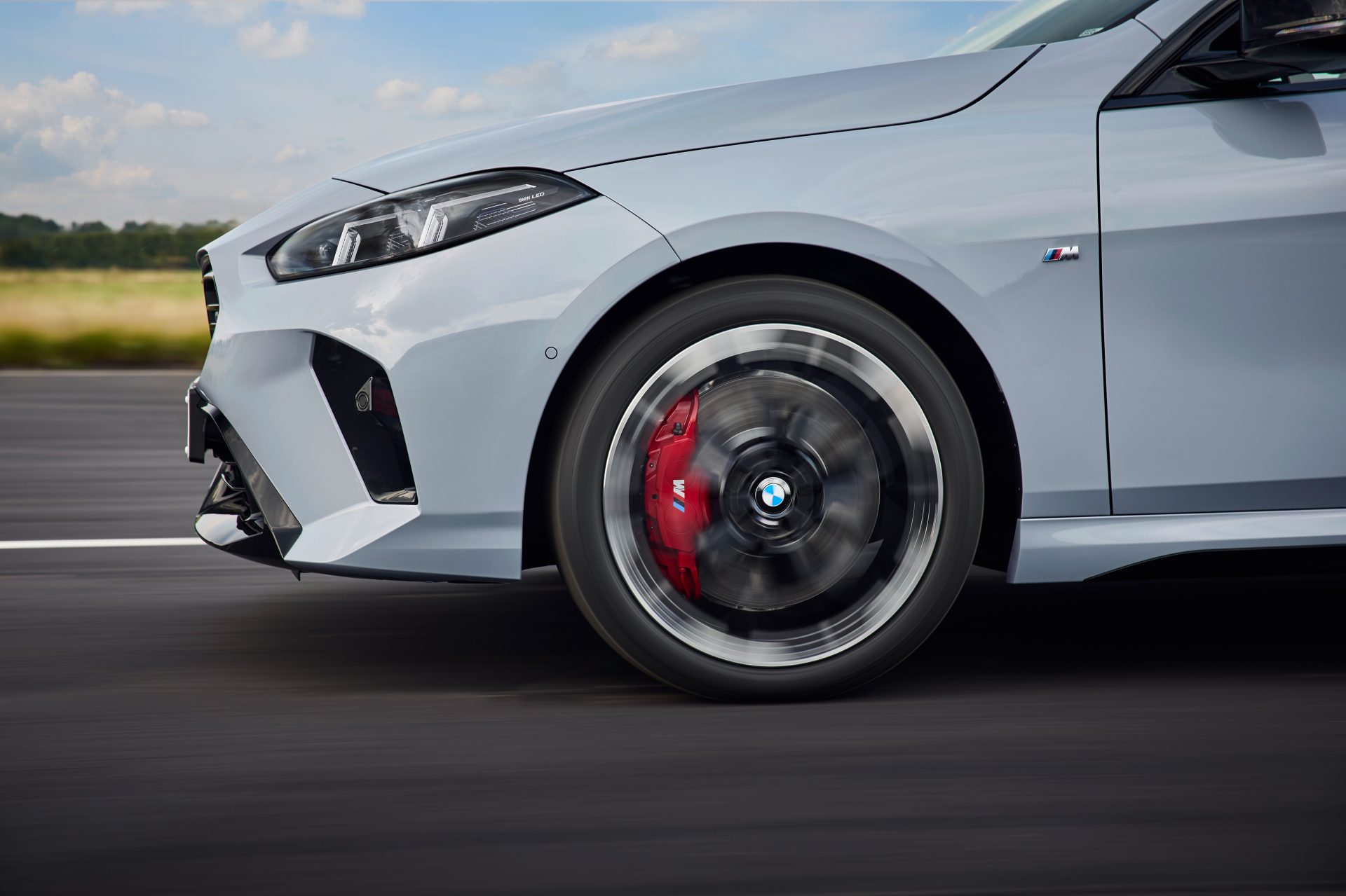 Front view of a moving BMW with focus on the red-painted brake system and spinning wheel on a country road.