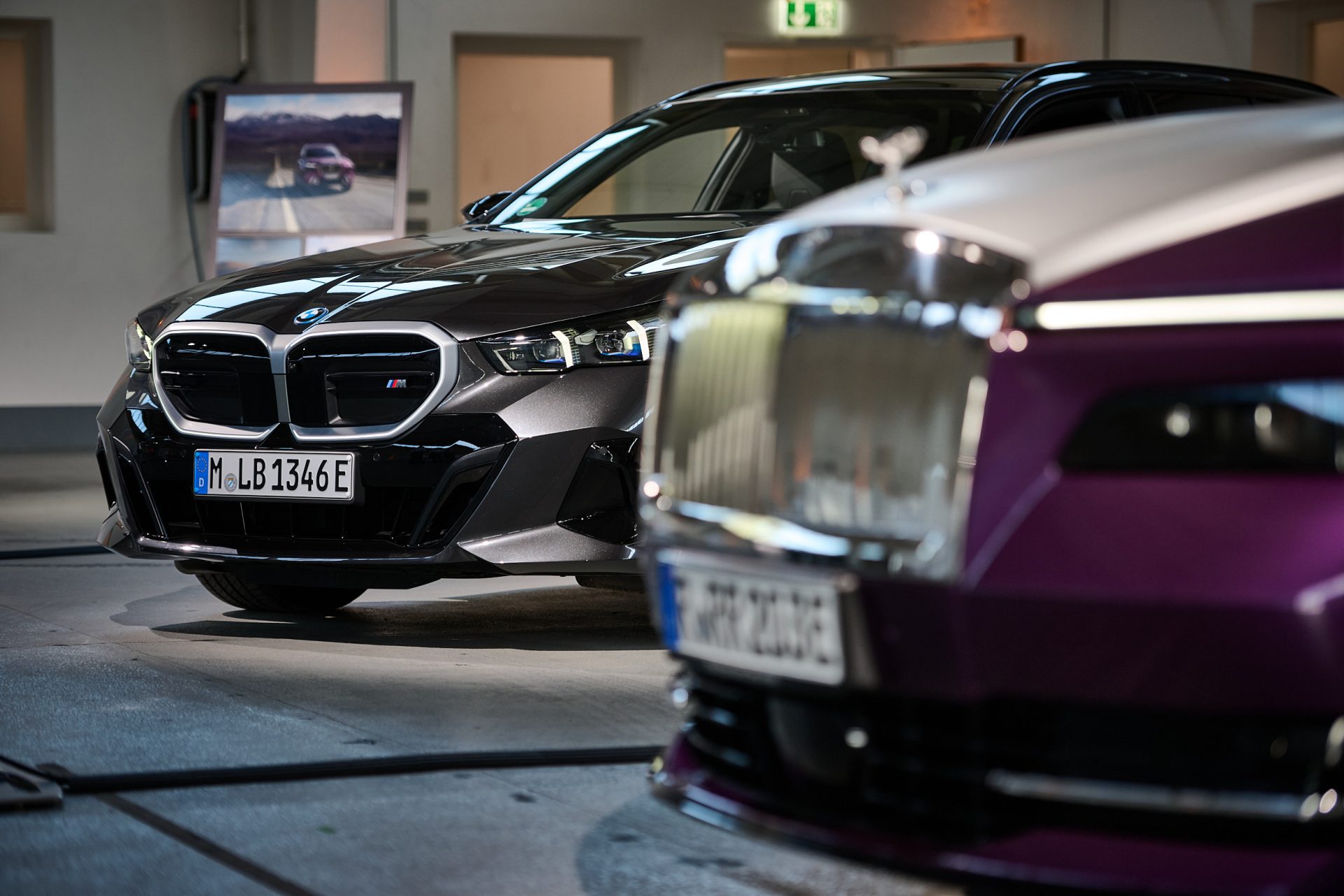 Front view of a black BMW and a purple-white Rolls-Royce in an indoor setting with a charging station in the background.