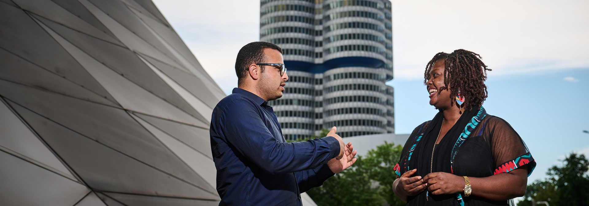 A man and a woman shake hands in front of the BMW building.