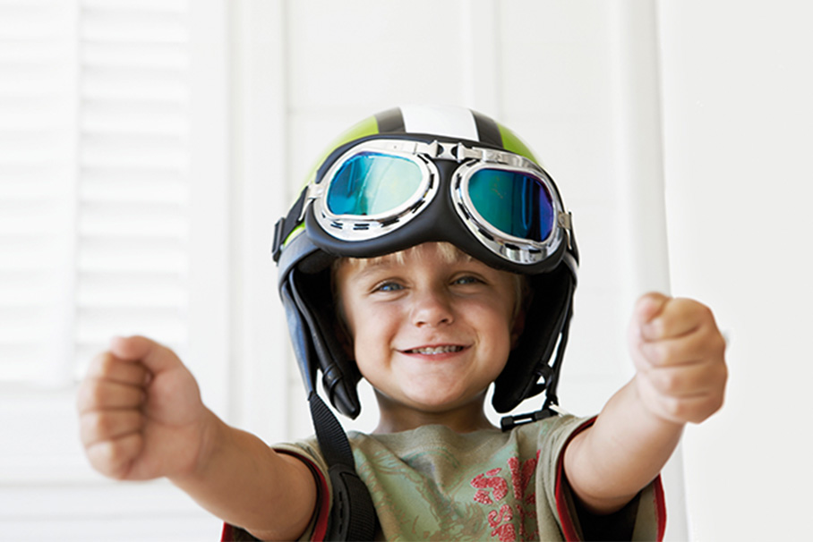 A child smiles at the camera while wearing a motorcycle helmet that is too big for the child