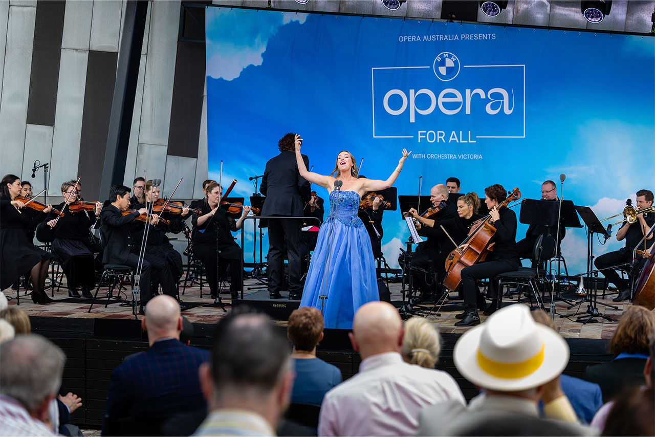 A woman in a blue dress siging on a stage with a orchestra in the background