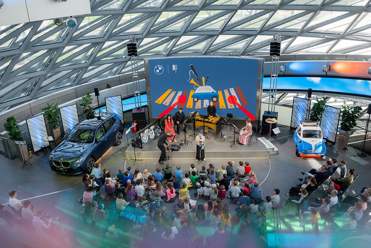 A concert for a smaller group of people. A modern BMW X3 and a historic Isetta are parked next to the stage