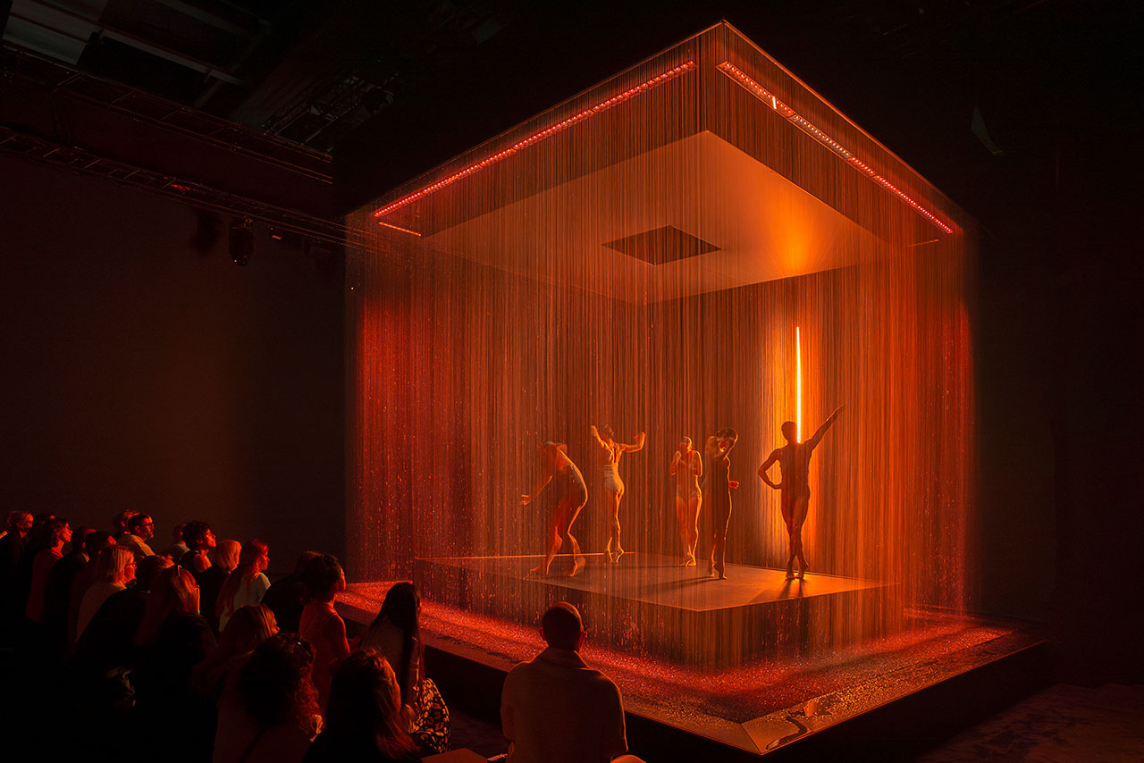 Four people in a performance behind a curtain on an orange-lit stage