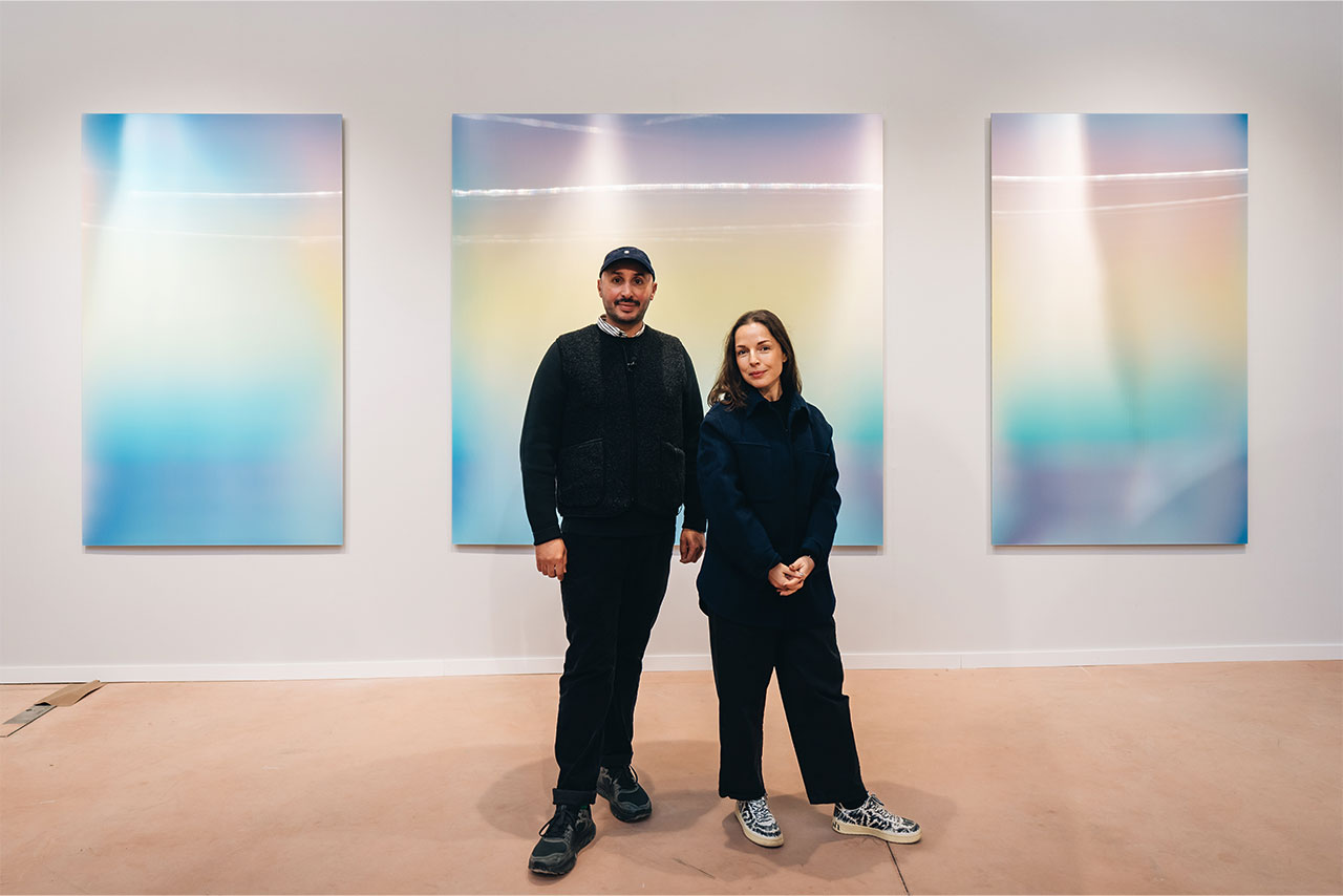 A man and a woman standing infront of three pastel-colored pictures.