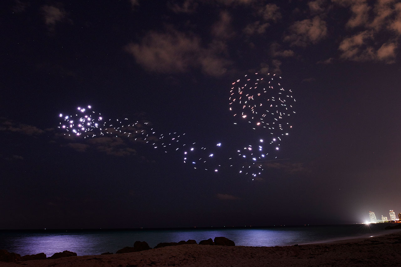 illuminated drones fly through the sky at night