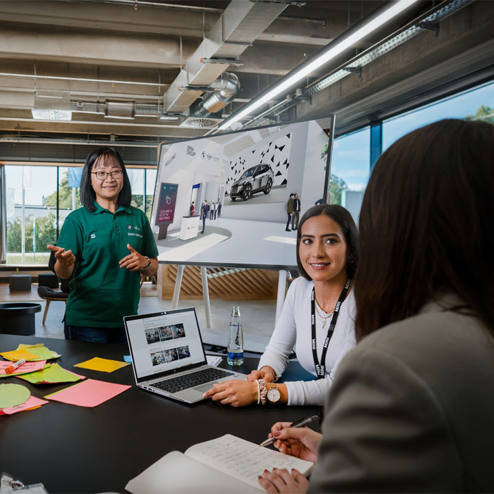 Several people gather around a table with a laptop on it.
