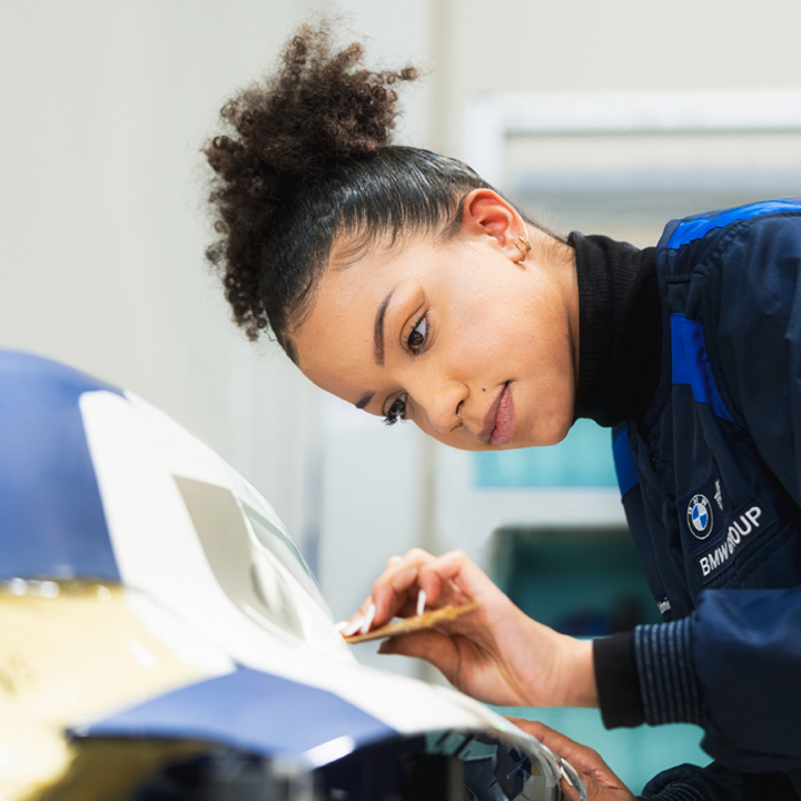A woman performs maintenance work on a car in a workshop.