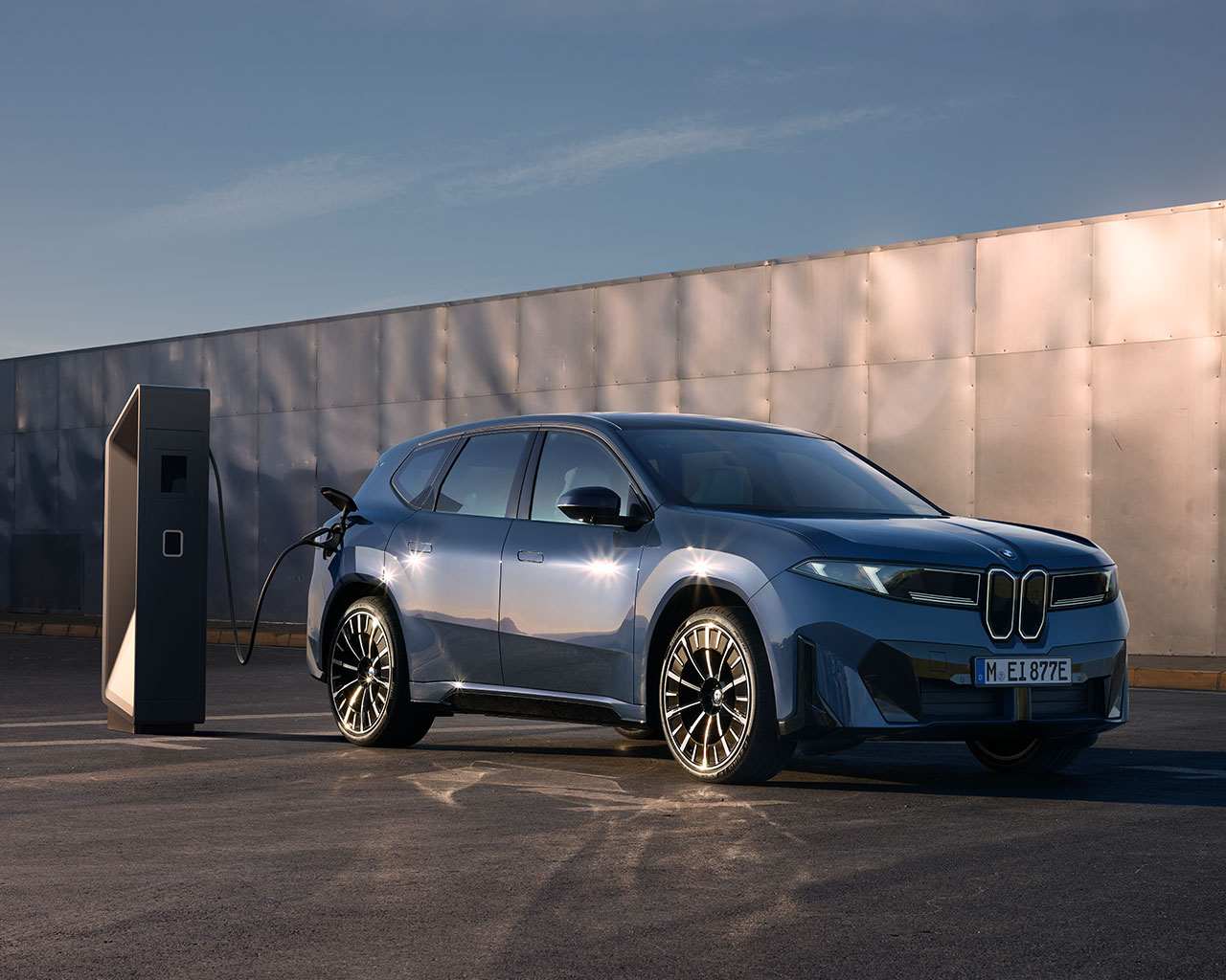 A BMW New Class is displayed on a charger standing on a platform in a natural environment.