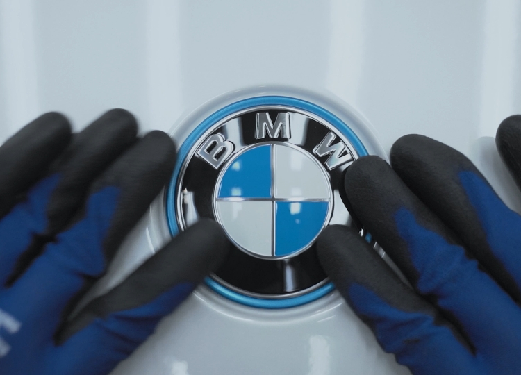 Zwei Hände in blauen Handschuhen berühren das BMW-Emblem.