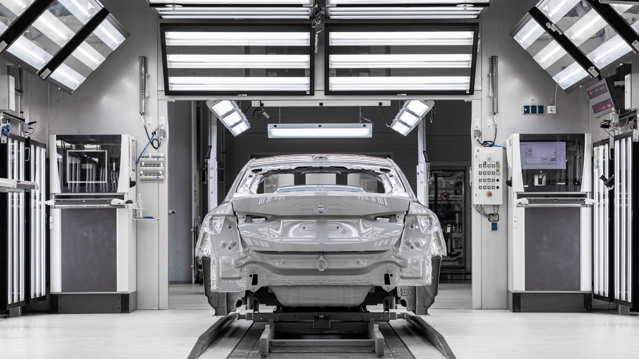 Silberne Autokarosserie auf einem Fertigungsstand, Blick auf das Heck, in einer Werkstattumgebung.