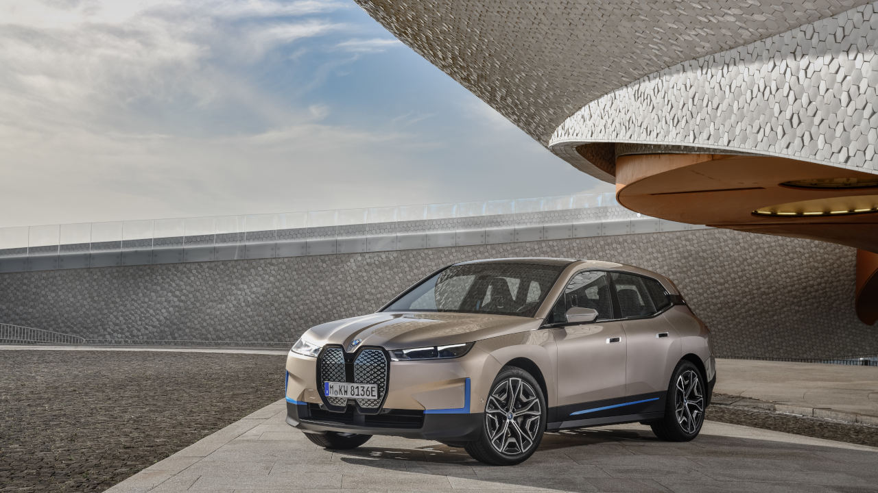 Ein BMW Elektro-SUV steht auf einer Betonfläche vor moderner Architektur mit geschwungener, strukturierter Dachform.