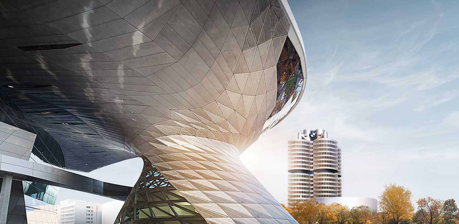 Im Vordergrund die BMW Welt mit markanter Metallfassade, im Hintergrund das BMW-Vierzylinderhochhaus mit Logo.