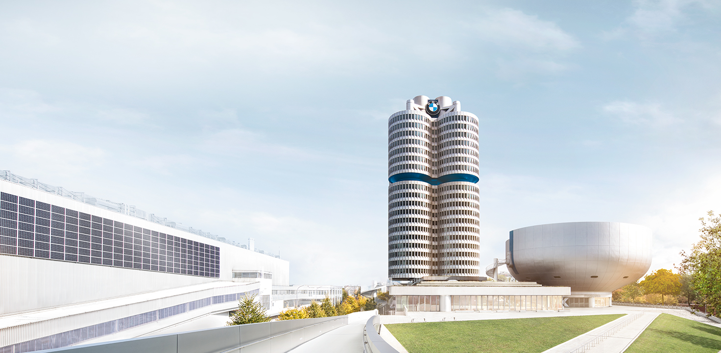 BMW-Vierzylinderhochhaus bei Tageslicht, umgeben von Produktions- und Ausstellungsgebäuden auf dem Münchner Werksgelände.