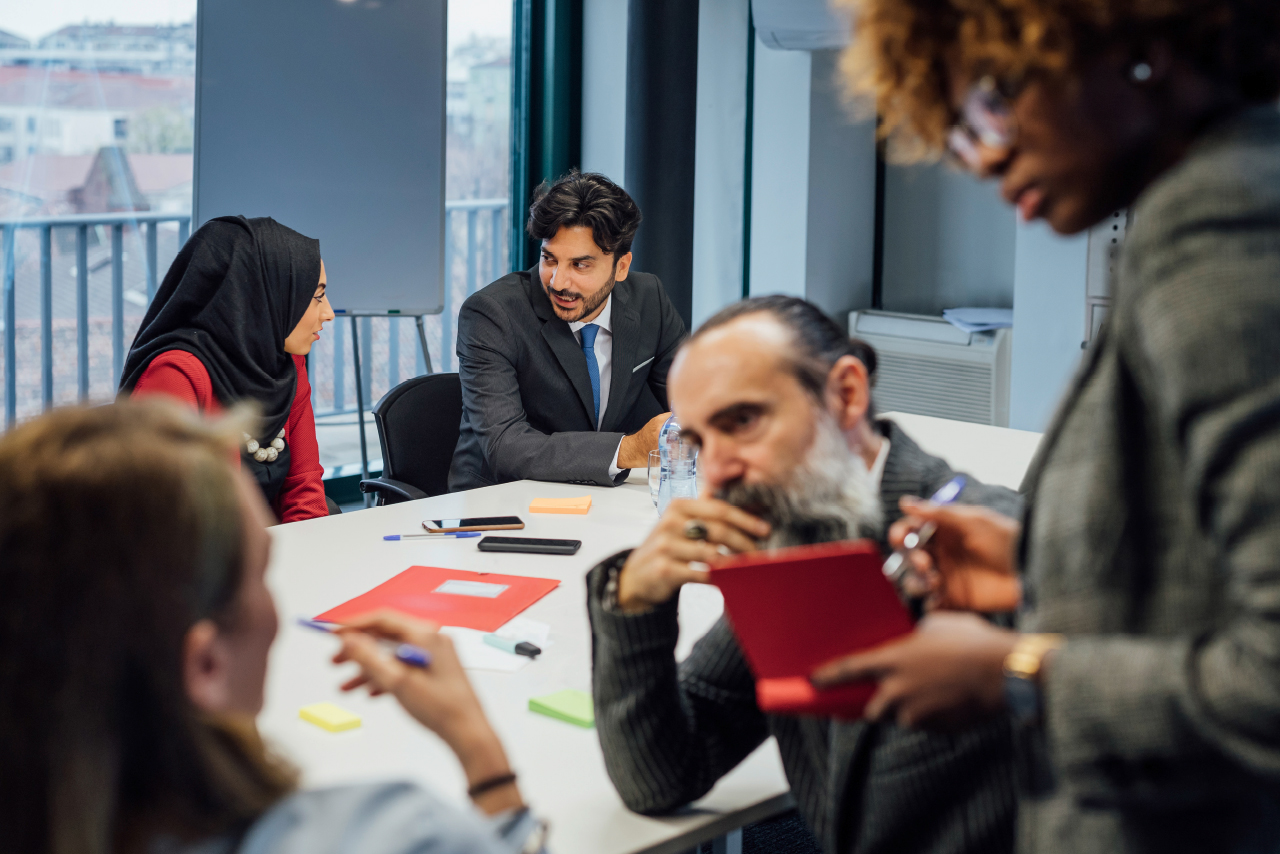 Teilnehmer einer Besprechung sitzen in einem Raum und tauschen Ideen aus.