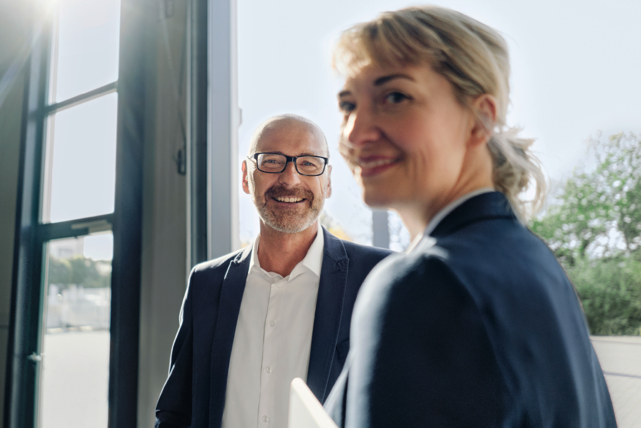 Mann und Frau stehen nebeneinander vor einem großen Fenster mit Blick auf die Umgebung.