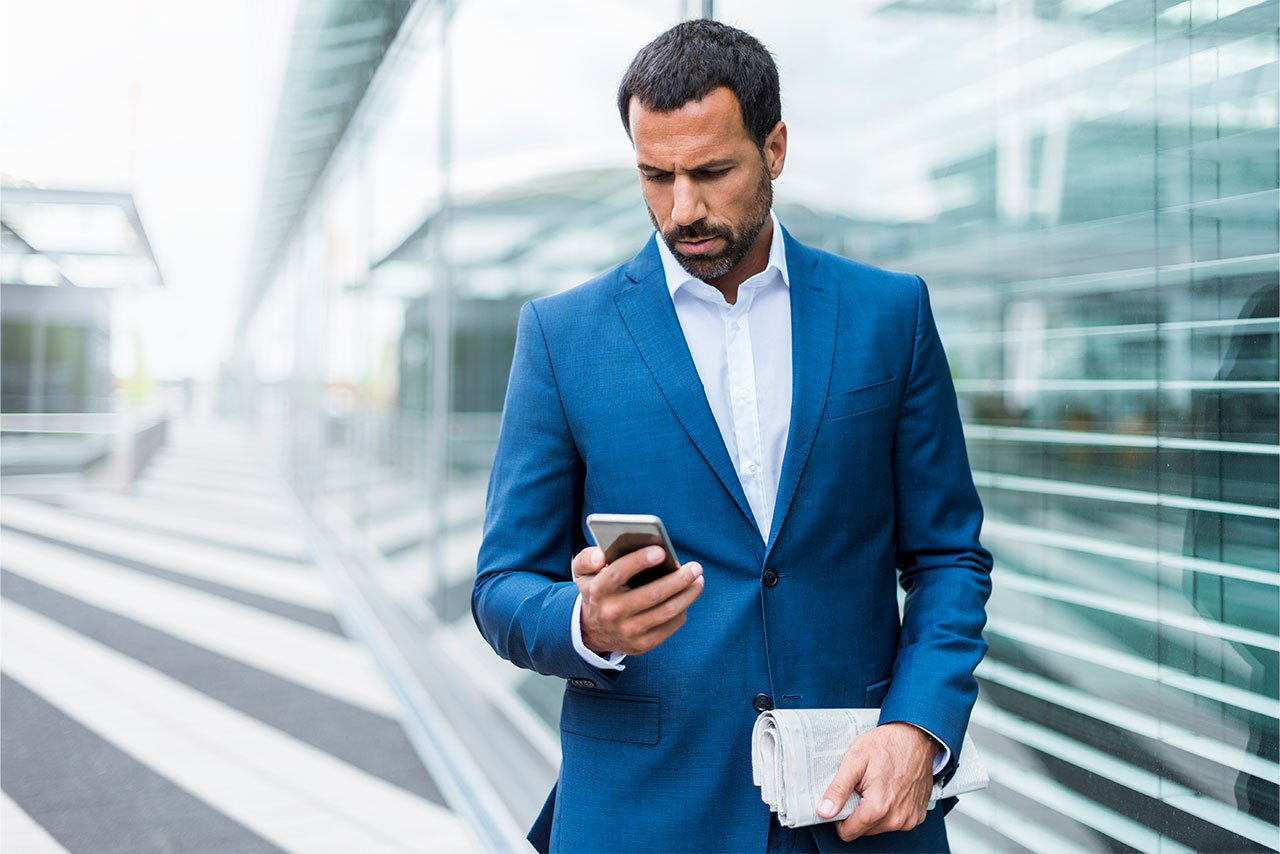 Ein Mann trägt einen blauen Anzug und betrachtet sein Mobiltelefon.