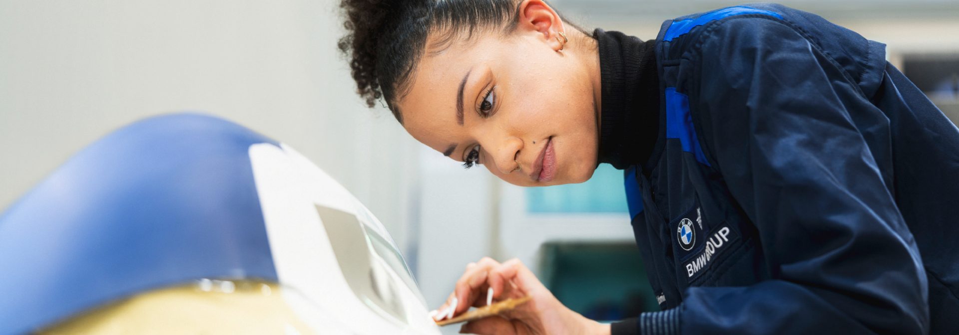 Eine Frau in blauer Jacke arbeitet daran, ein Auto zu streichen.