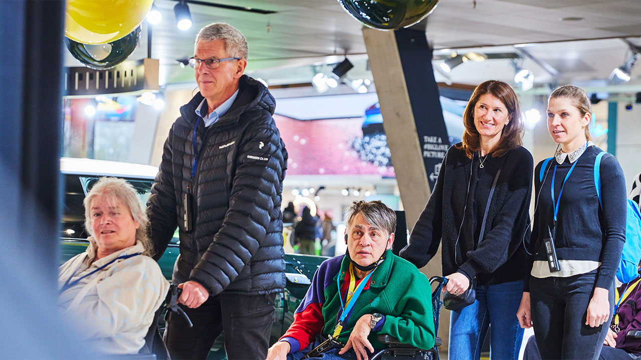 Eine Gruppe von Menschen steht lächelnd vor einem großen Foto, das sie abbildet.