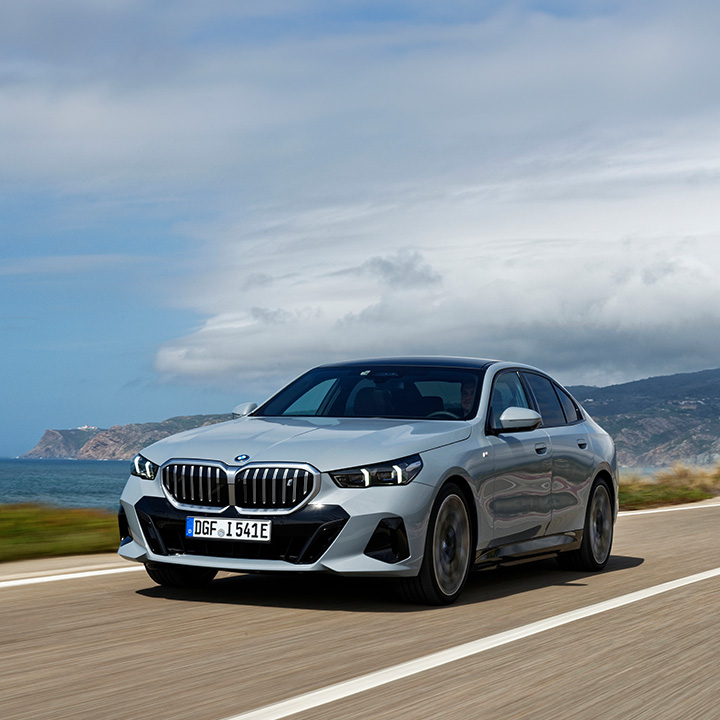 BMW i5 fährt auf einer Landstraße, im Hintergrund ist das Meer zu sehen.