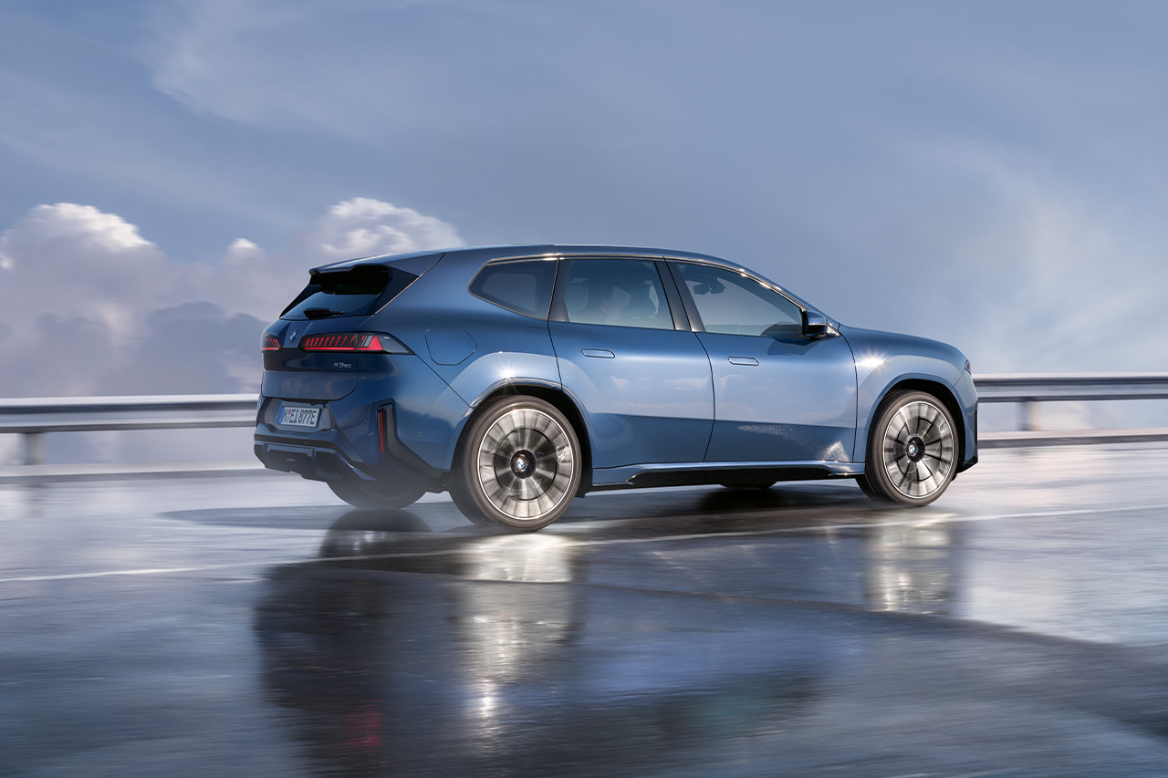 Dunkelblauer BMW iX3 fährt auf nasser Fahrbahn.