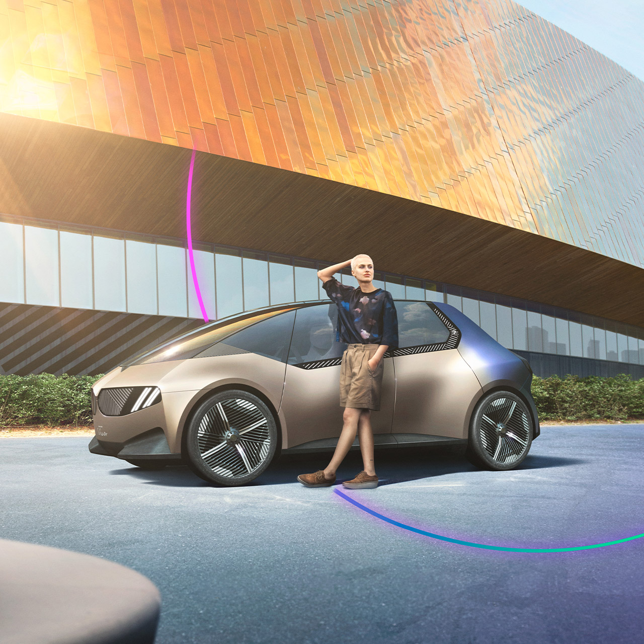 Gold-farbener BMW i Vision Circular vor einem hoch modernen Gebäude, eine Person lehnt sich an dem Fahrzeug an.