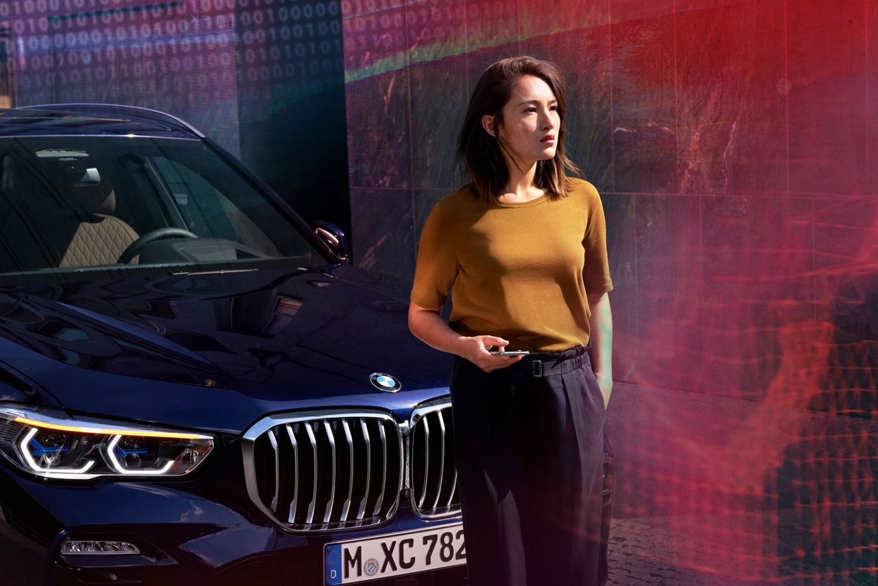 A woman stands in front of her BMW and holds a smartphone in her hand.
