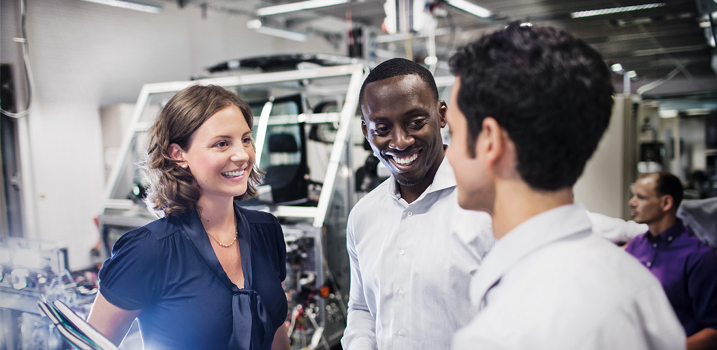 Three different BMW employees standing together in production environmet having a conversation.