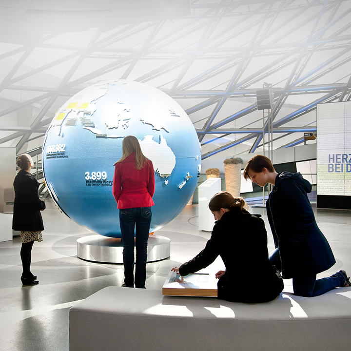 Several people in front of a globe within the double cone of the BMW World.