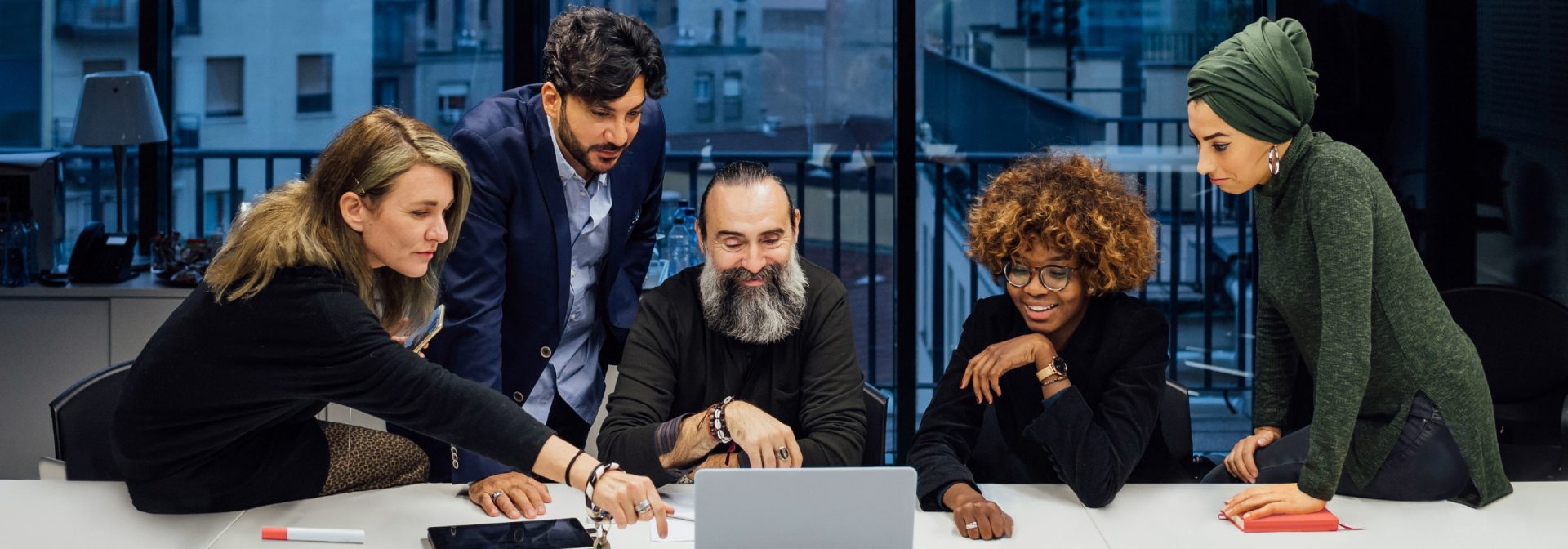 Five people standing together around a computer and talk about something.